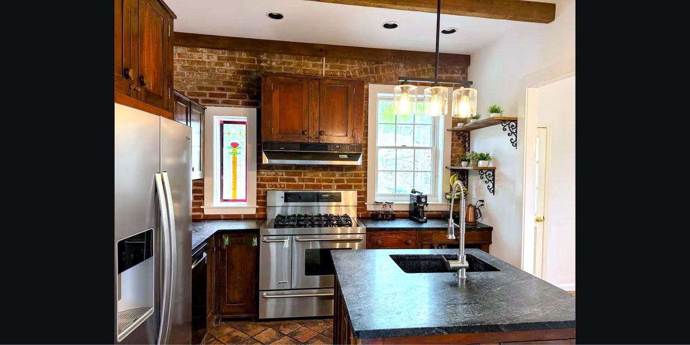 Kitchen with exposed brick wall, soapstone island, and pendant lights