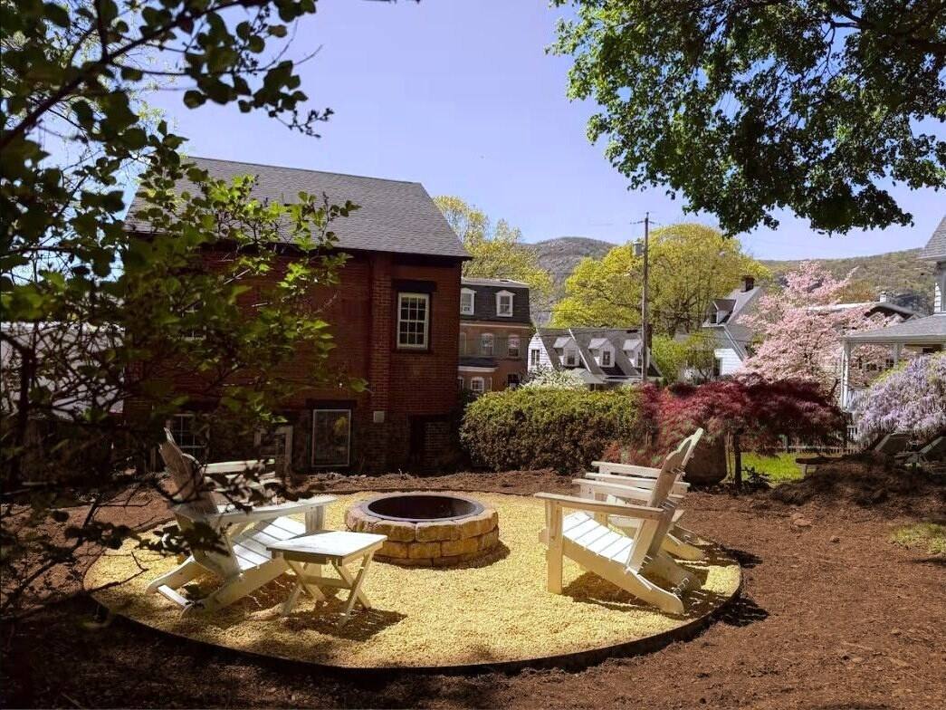 Backyard fire pit with white Adirondack chairs under the trees