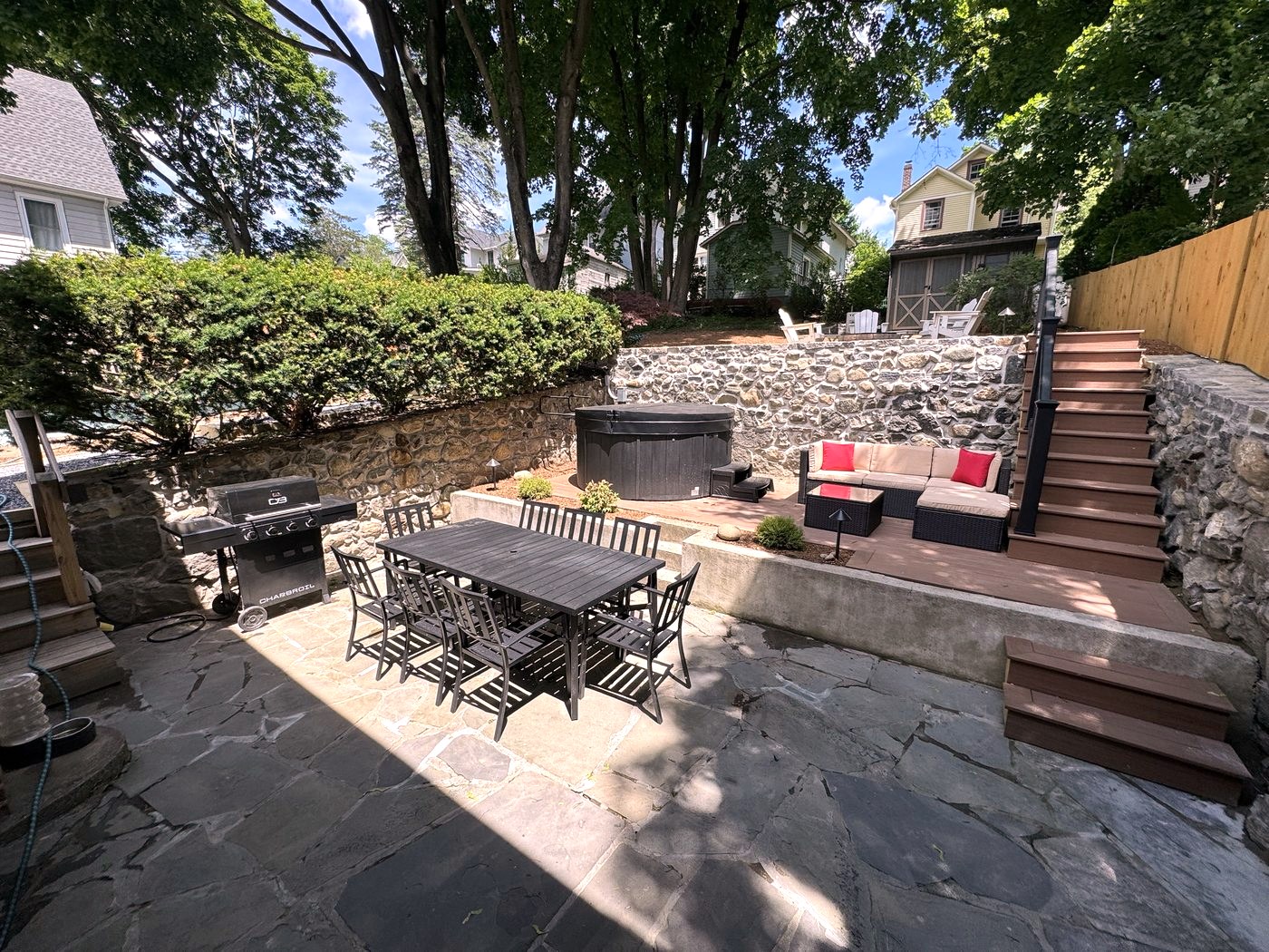 Stone patio with dining table, gas grill, and steps up to the hot tub and lounge area