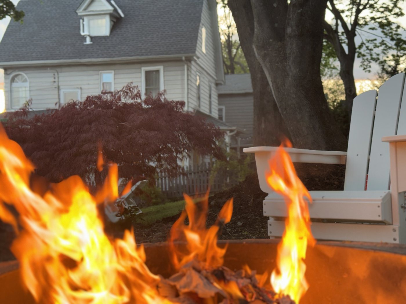 Close-up of fire pit flames at dusk with an Adirondack chair beyond